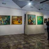 Sala wystawowa, na ścianach wiszą obrazy z postaciami. Po prawej stoją dwie osoby przyglądające się obrazom.